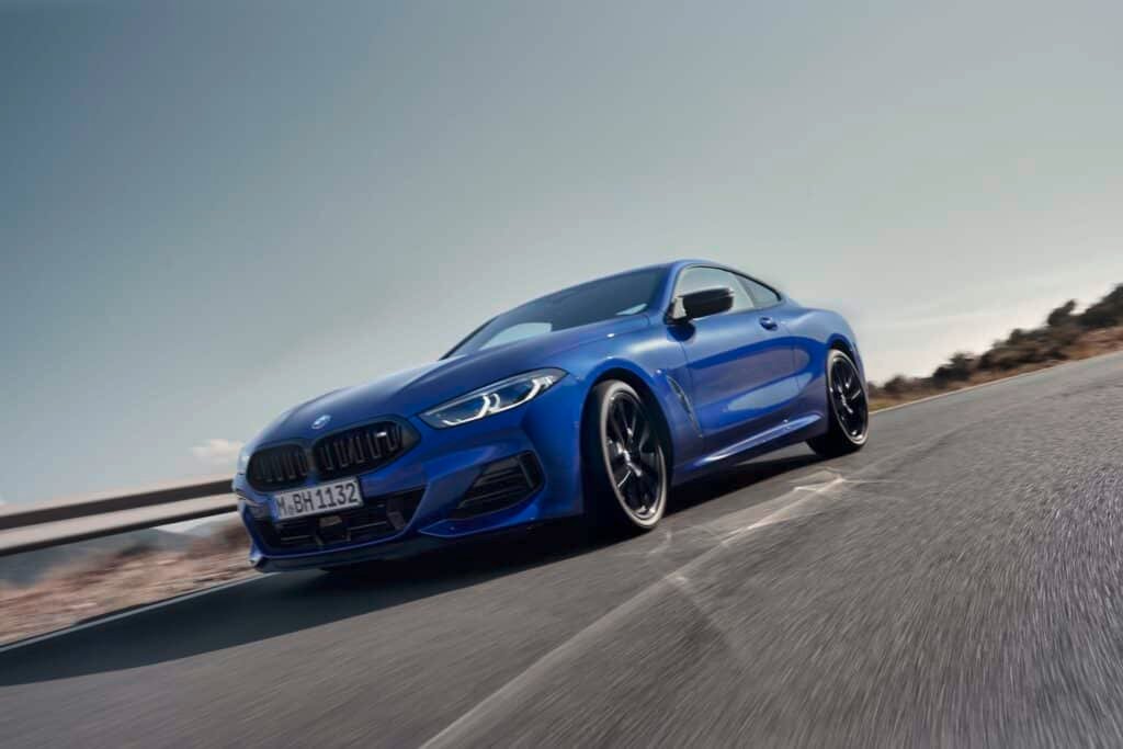 Front view of 2026 BMW 8 Series Coupe in Frozen Portimao Blue driving along coastal highway